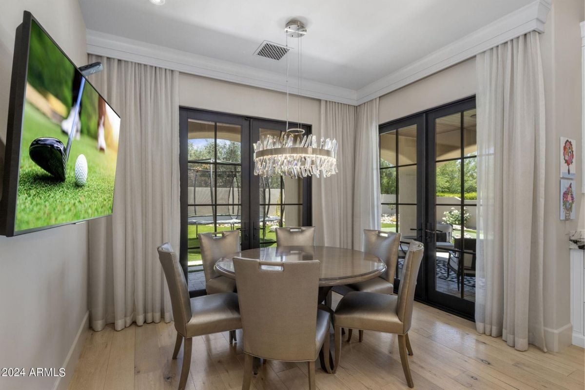 A breakfast nook with a TV, chandelier, and a round table surrounded by chairs.
