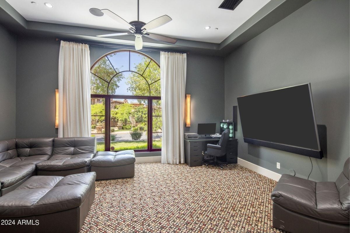 A media room with a TV, couch, desk, chair, and ceiling fan.