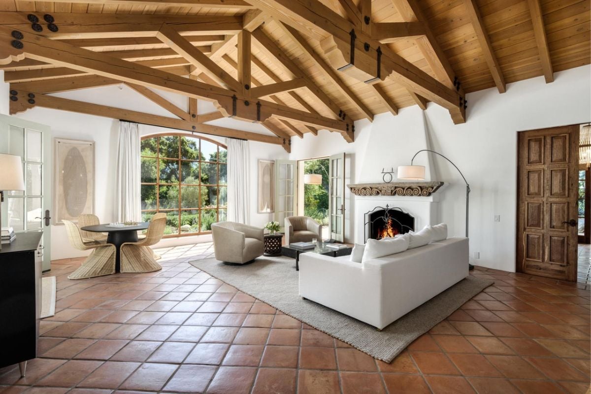 A living room with a fireplace, exposed beam ceiling, couches, and a center table.