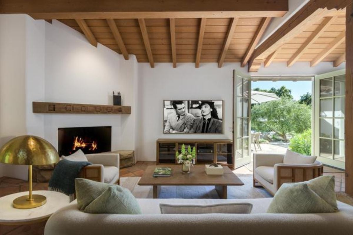 A living room with a TV, fireplace, exposed beam ceiling, couches, and a coffee table.