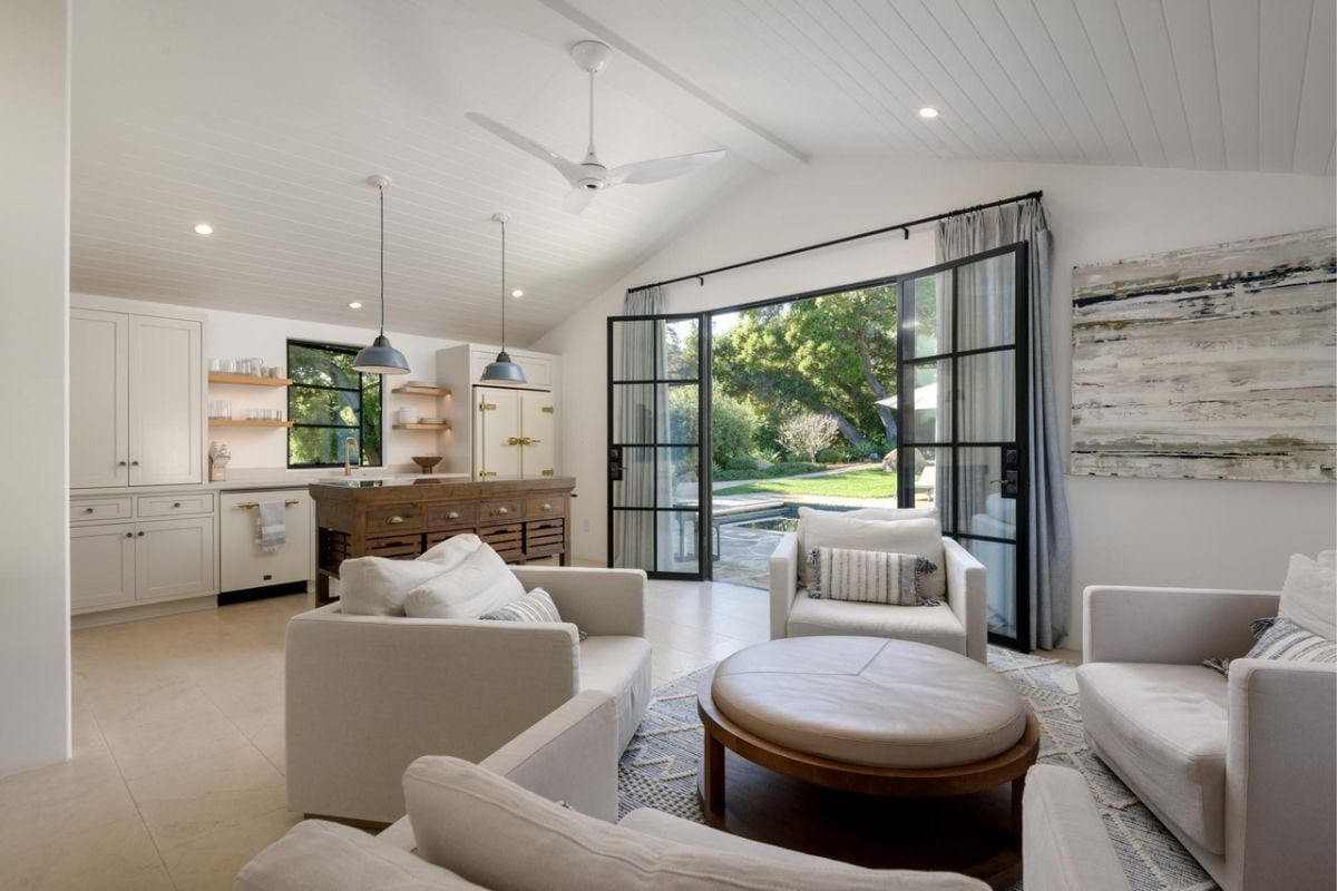 A living space that is part of the great room, with white couches, a center table, a white ceiling, and a ceiling fan.