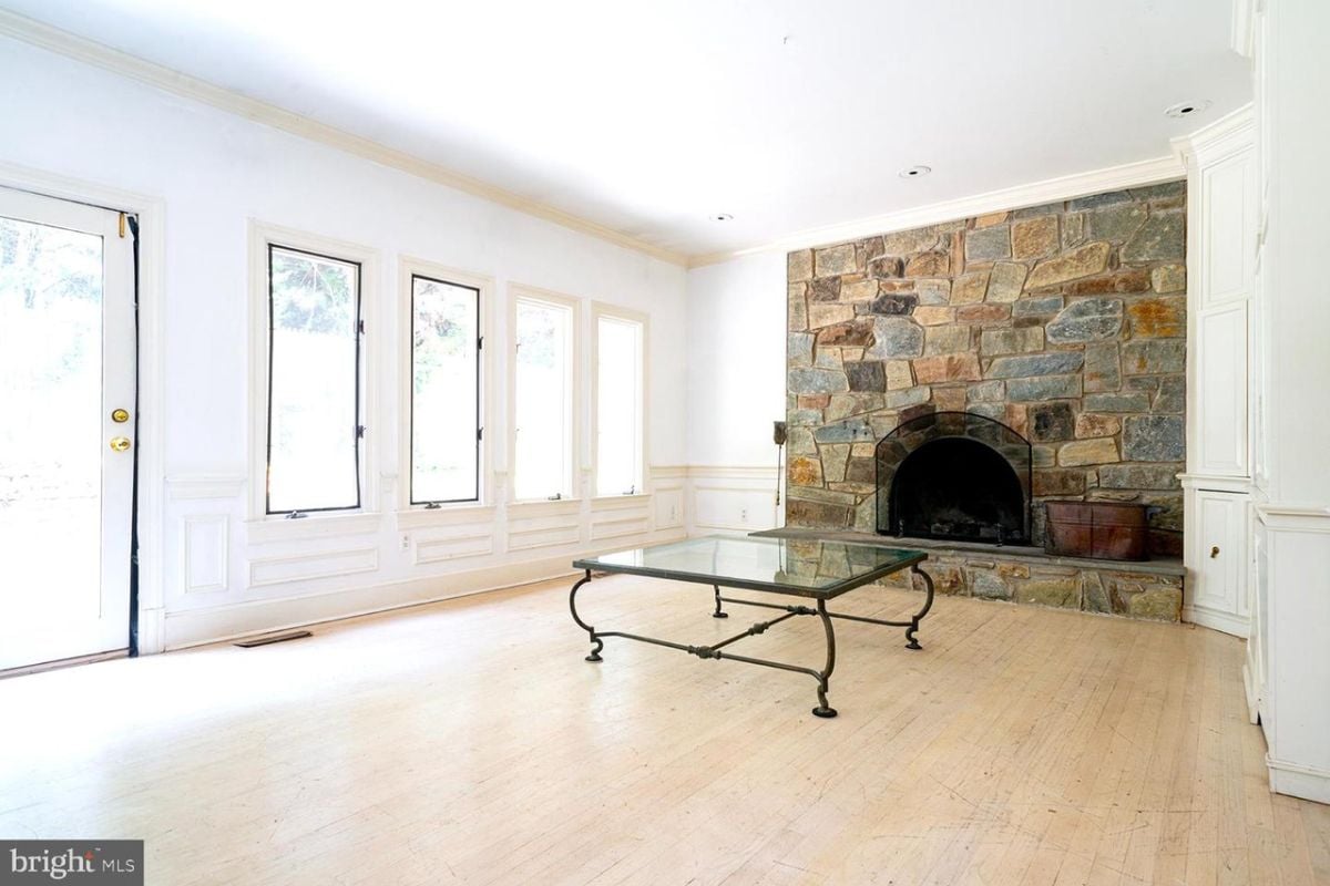 A living room with windows, a stone fireplace, and a glass center table.