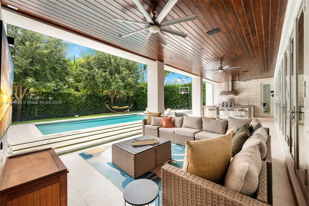 A porch with couches, pillows, a wooden ceiling, and a ceiling fan.