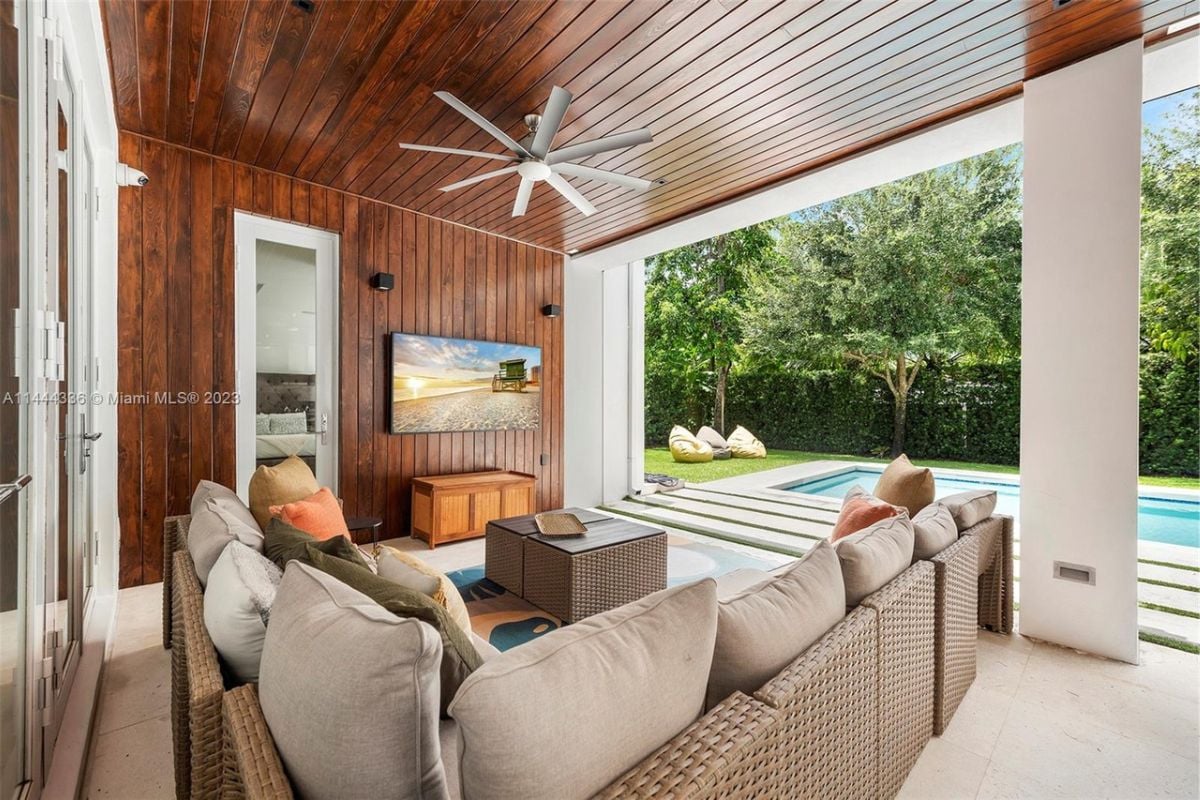 A porch with couches, pillows, a wooden ceiling, and a ceiling fan.