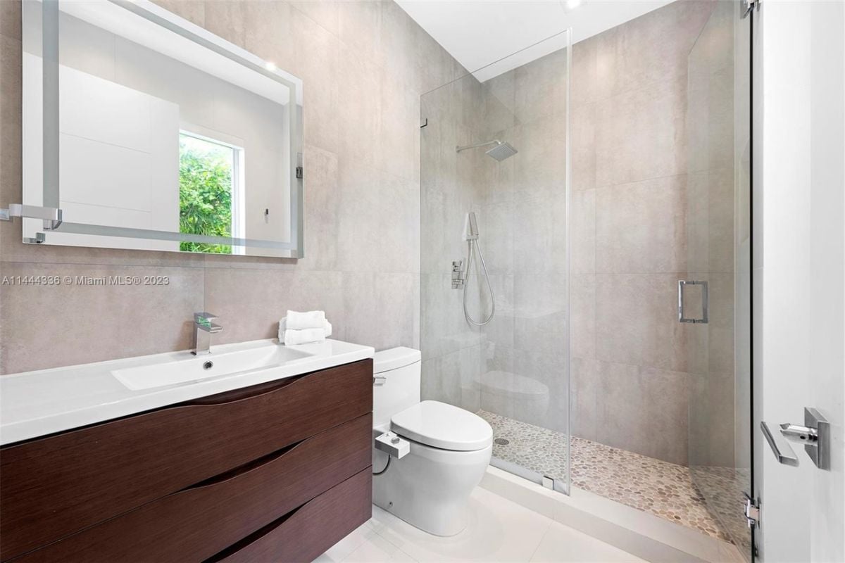 A bathroom with a vanity, window, toilet, and shower room.