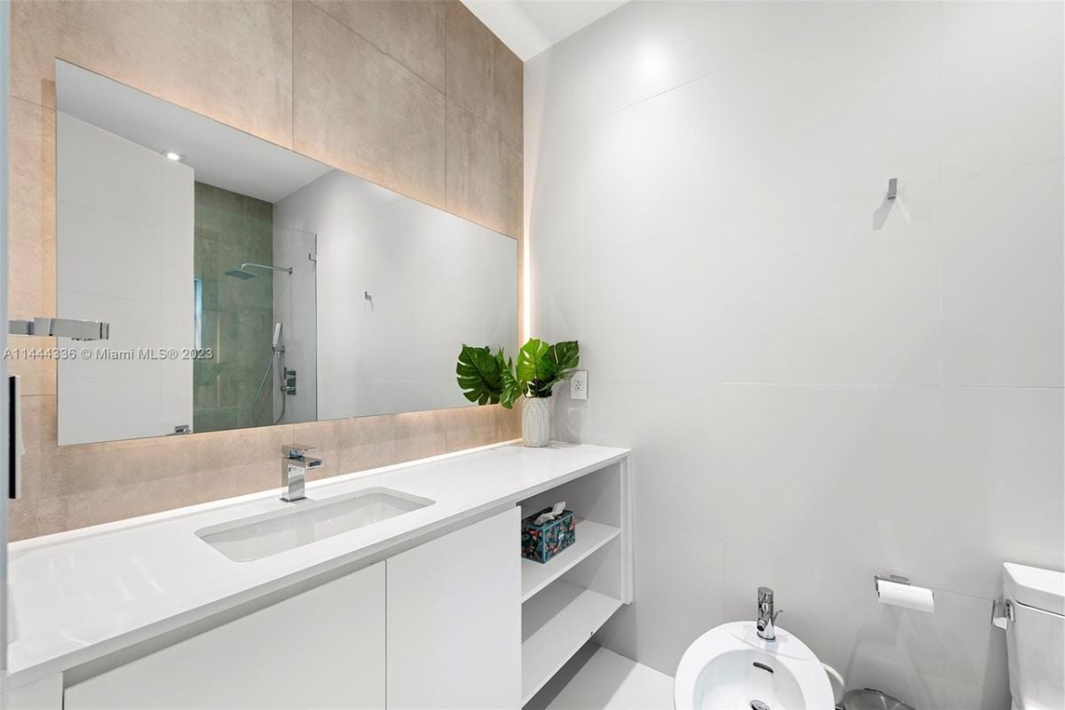 A bathroom with a white vanity, mirrors, toilet, and white cabinet.