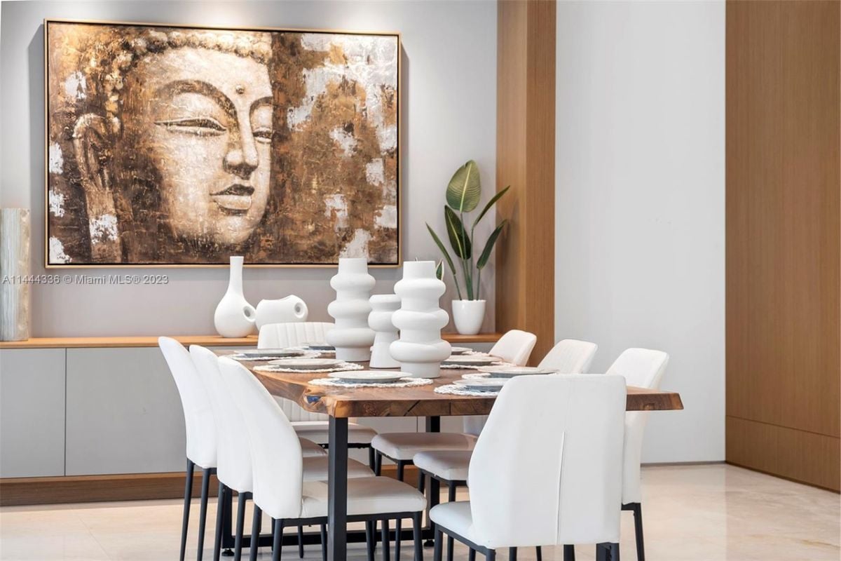 A dining room with a painting and a dining table surrounded by white chairs.