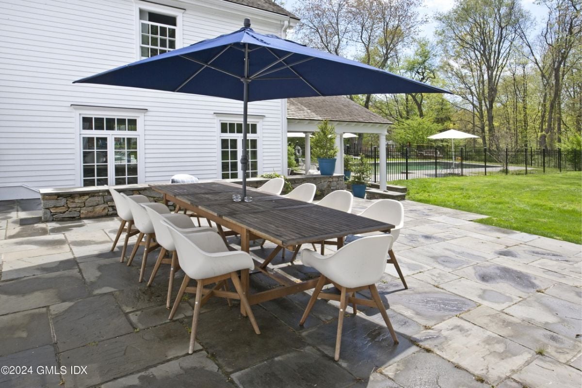 A patio with an umbrella and a table surrounded by chairs.