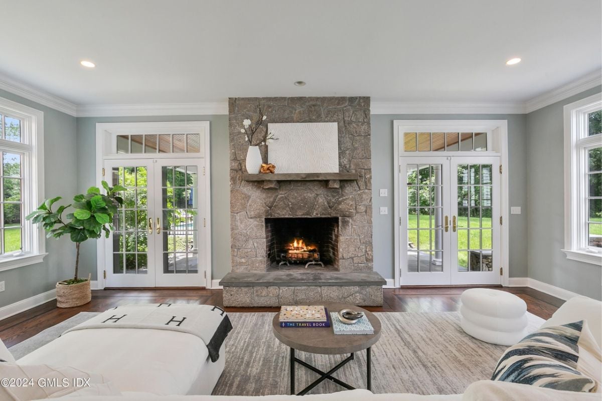A living room with a fireplace, painting, mirror, windows, couches, houseplant, and a center table.