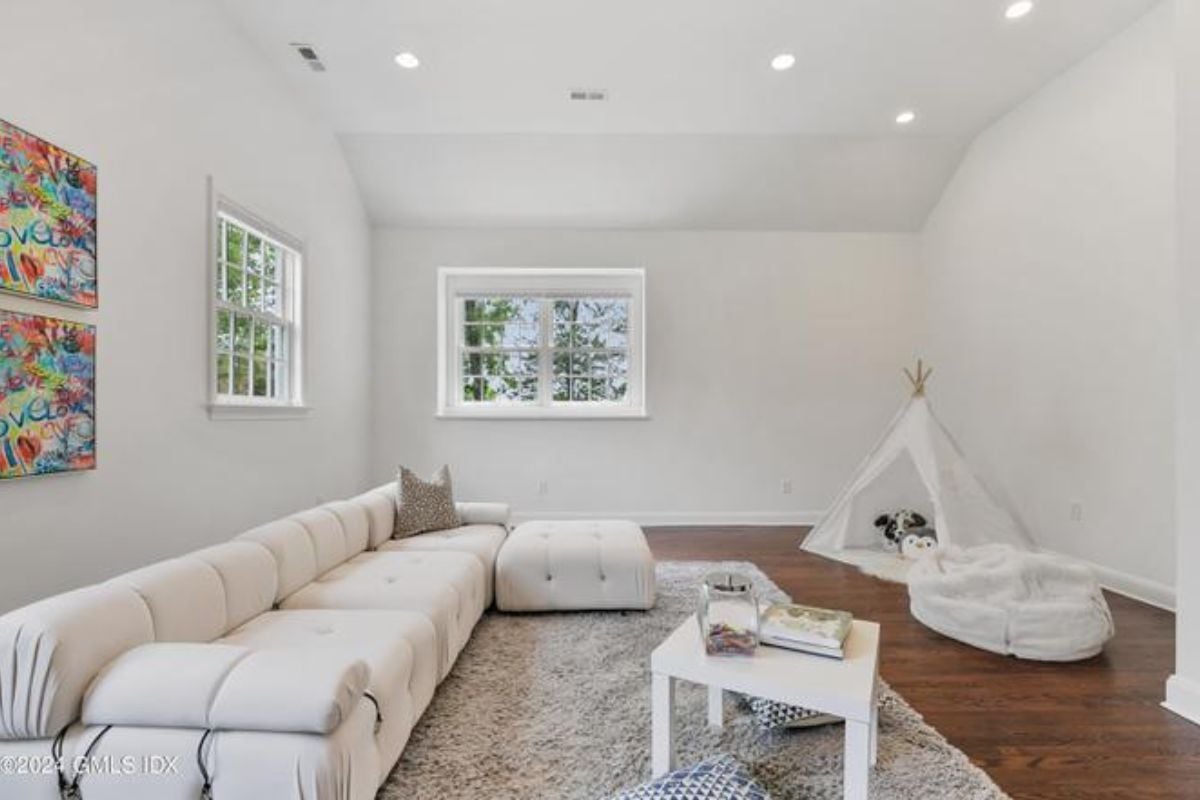 A lounge with windows, paintings, a white couch, and a coffee table.