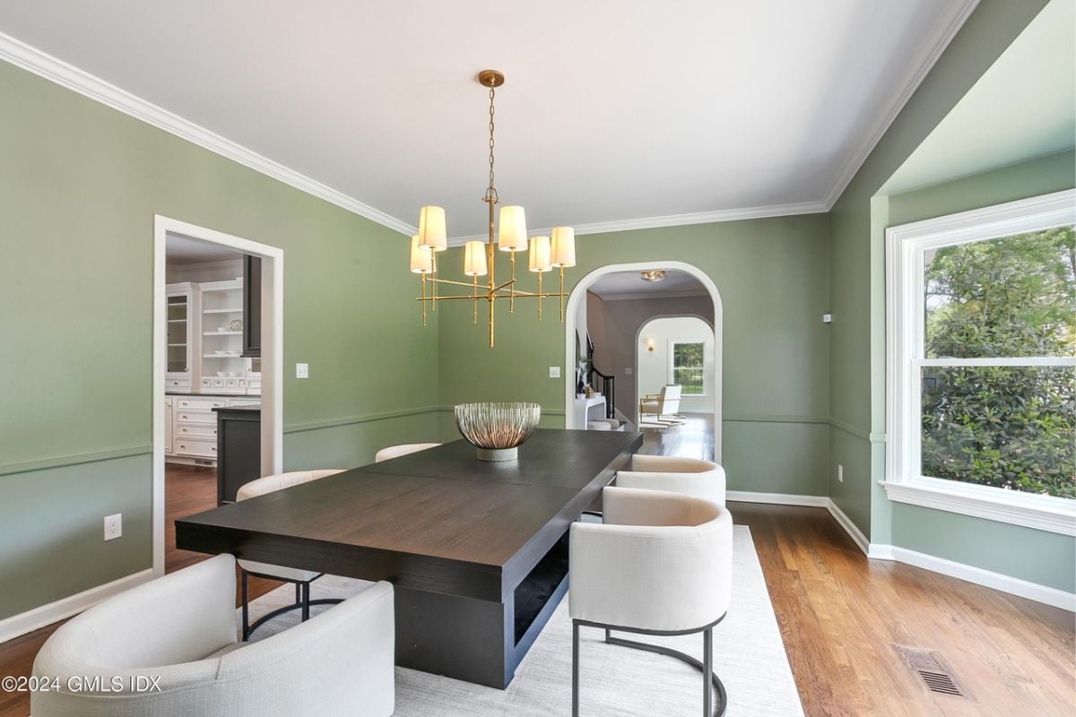 A dining room with green walls and a dining table surrounded by chairs.