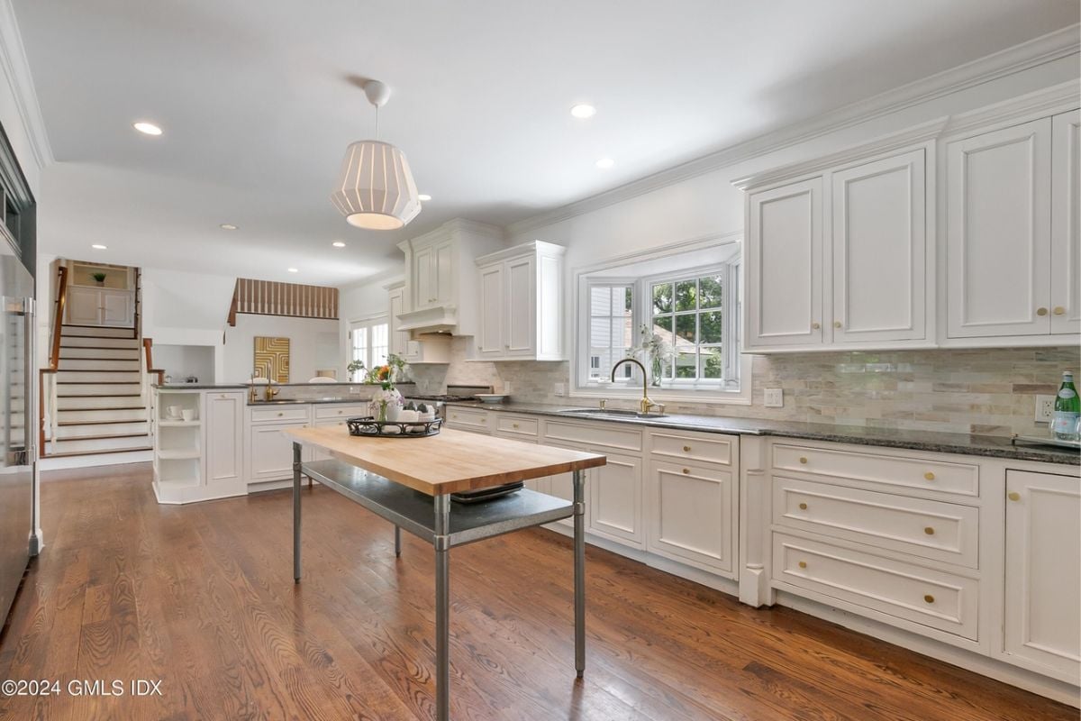 A kitchen with a wooden floor, center table, countertops, sink, and cabinets.
