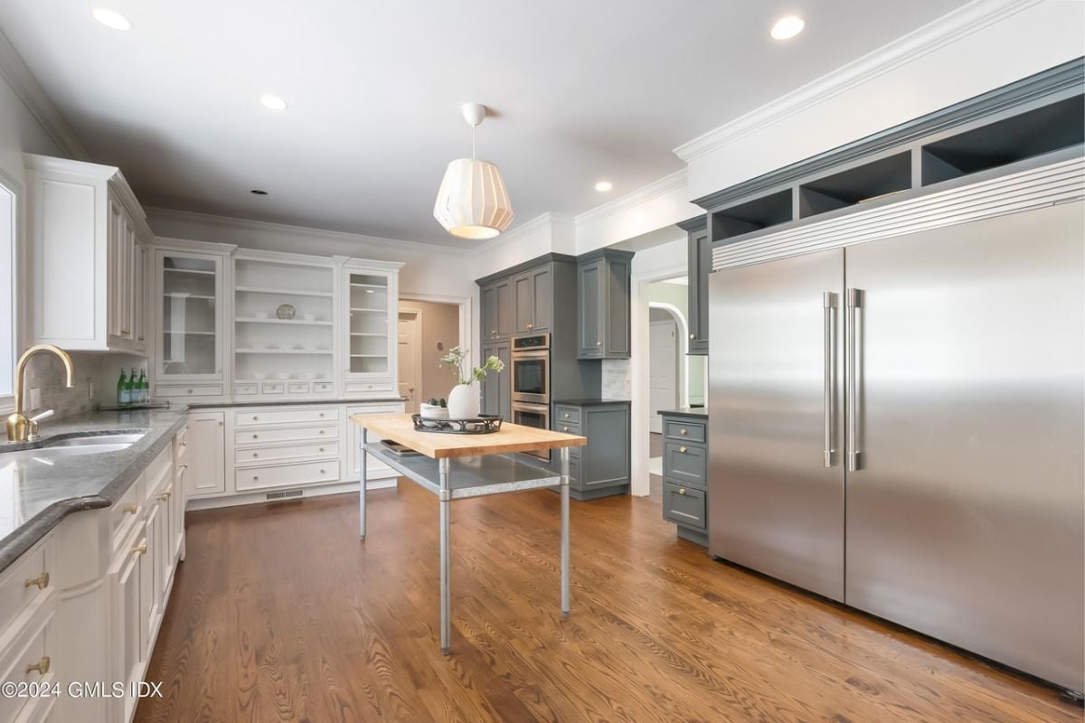A kitchen with a wooden floor, center table, countertops, sink, and cabinets.