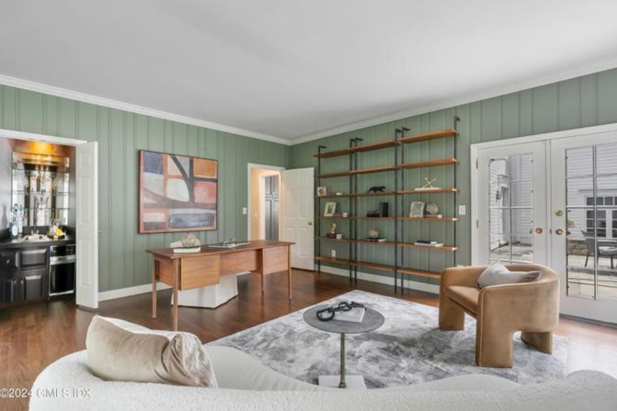 A home office with a rug, couch, shelves, painting, desk, and chair.