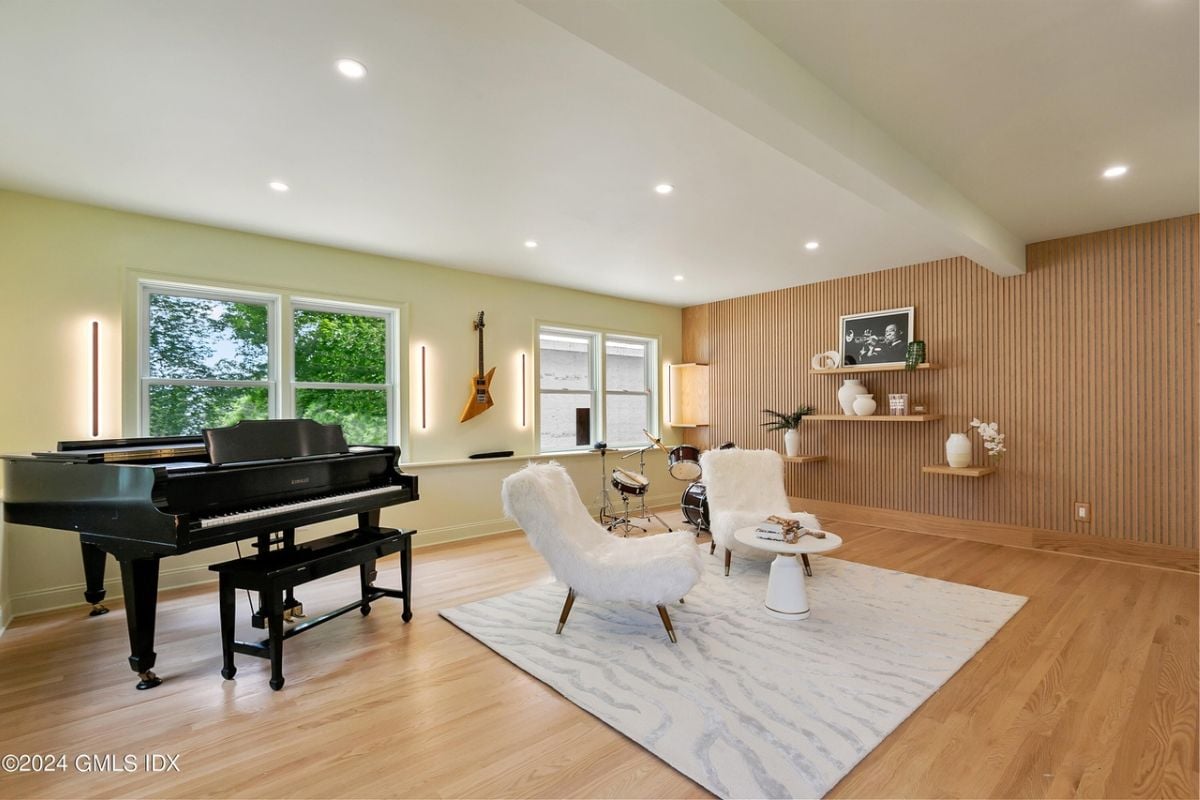 A music room with windows, a piano, rug, chairs, and a coffee table.