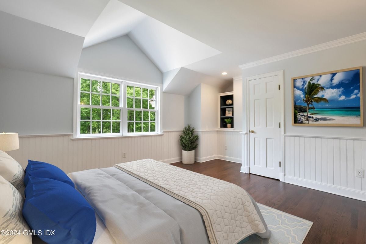 A bedroom with a bed, window, painting, and a white ceiling.