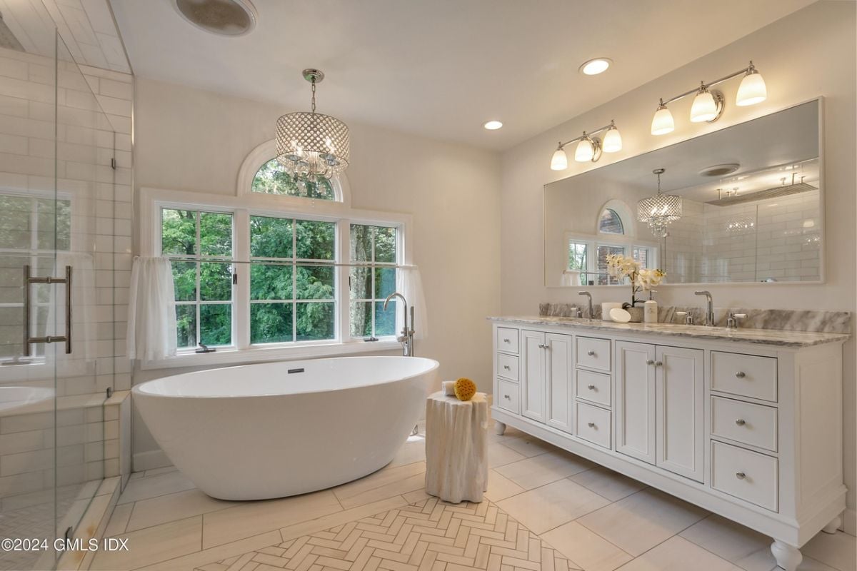 A bathroom with a bathtub, countertop, sink, mirror, cabinets, and a window.