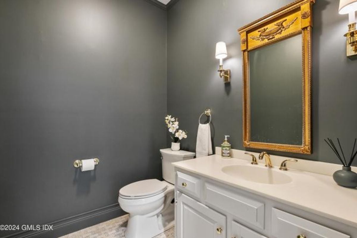 A bathroom with black walls, countertop, sink, mirror, and toilet.