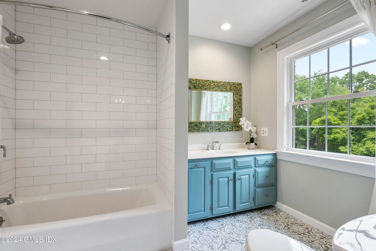 A bathroom with a countertop, cabinets, windows, a mirror, and a bathtub.