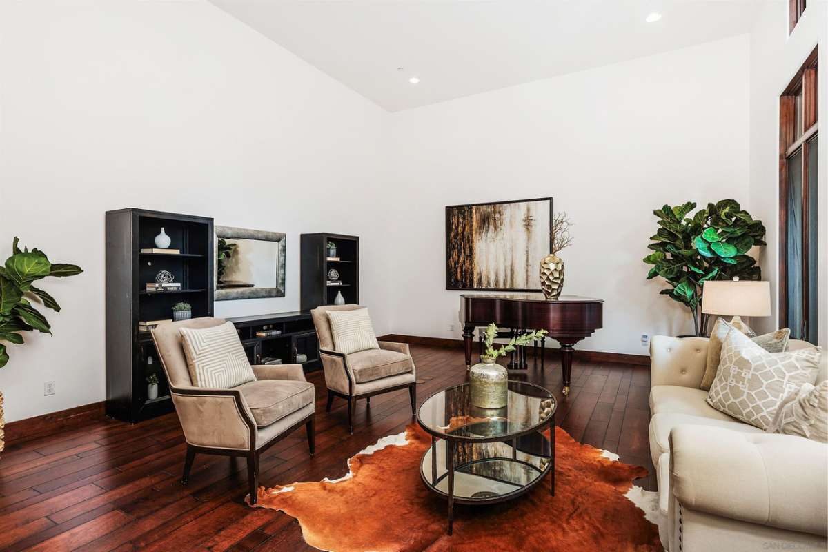 A living room with chairs, a couch, a piano, a painting, a houseplant, and shelves.