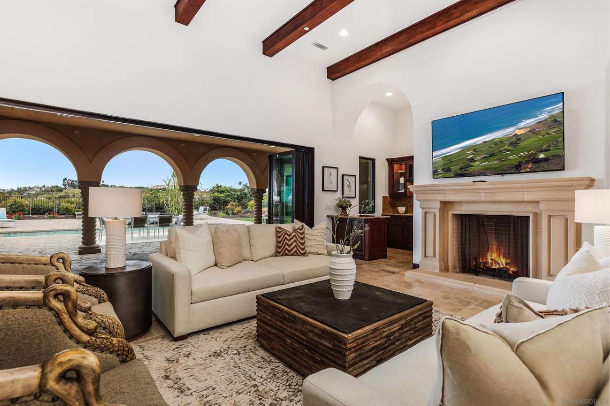 A living room with a fireplace, beamed ceiling, couches, a TV, and a coffee table with a vase.