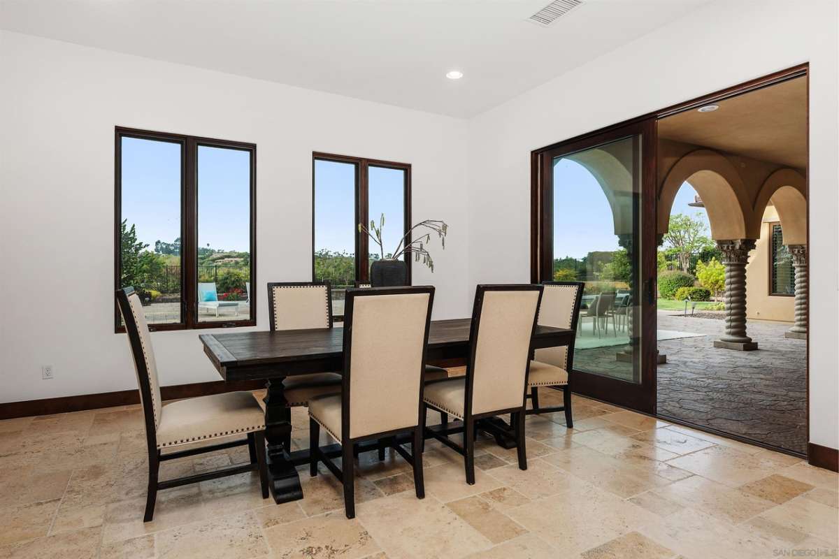 A dining room with a tiled floor, windows, and a dining table surrounded by chairs.