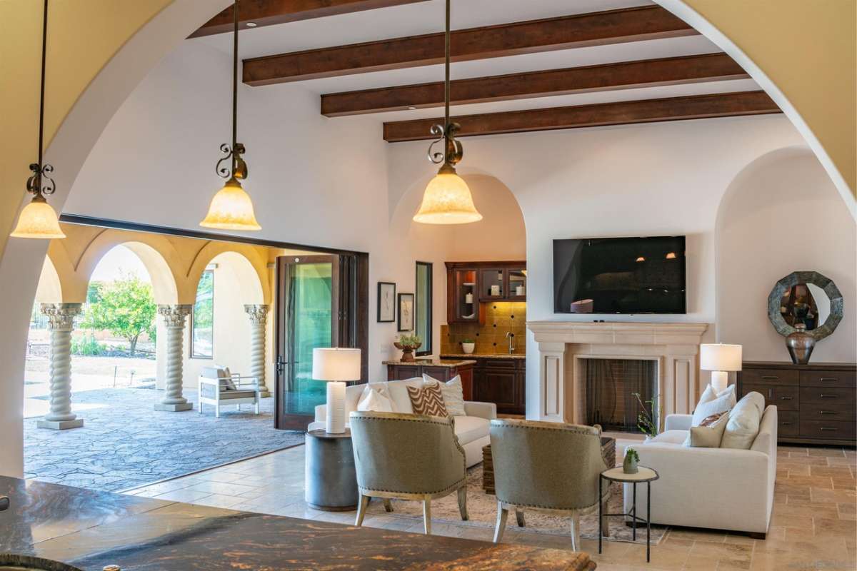 A living room with a beamed ceiling, fireplace, TV, couches, and chairs.
