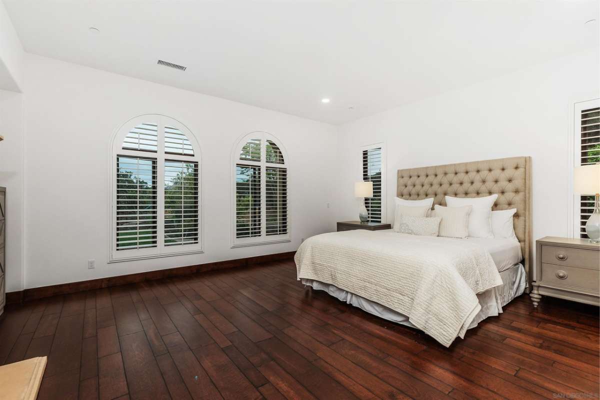 A bedroom with a bed, hardwood floor, windows, white ceiling, and nightstand.