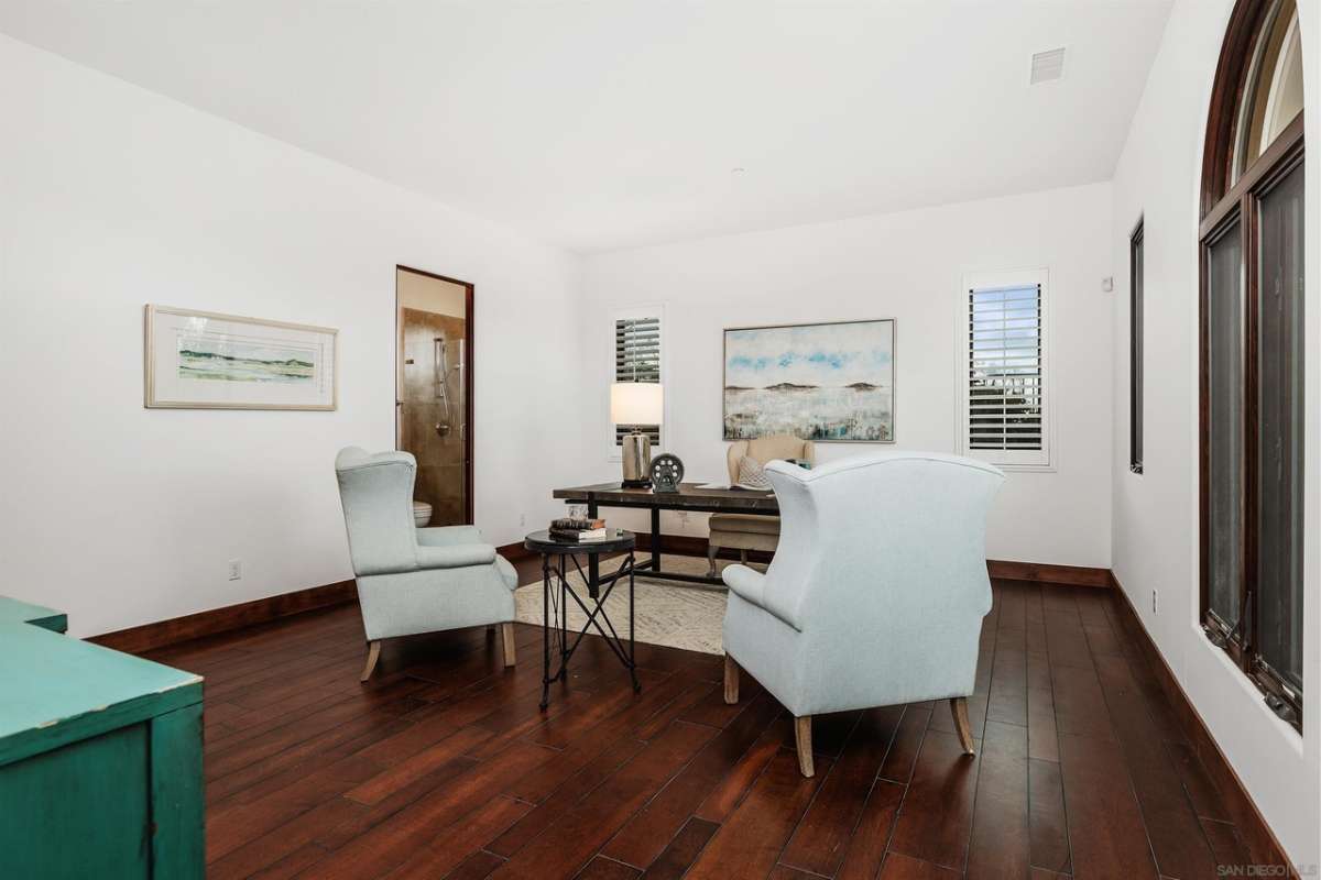 A home office with hardwood floors, paintings, windows, a white ceiling, desk, and chairs.