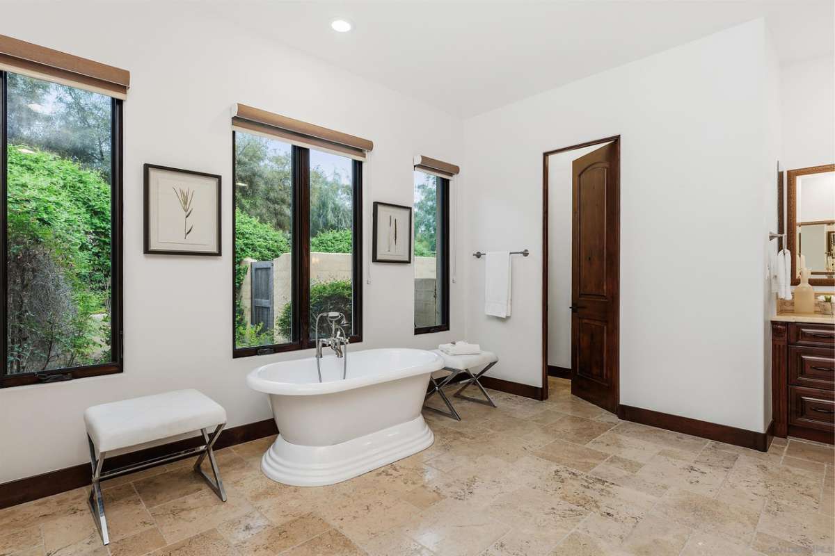 A bathroom with tiled floors, a bathtub, windows, and white ceiling and walls.