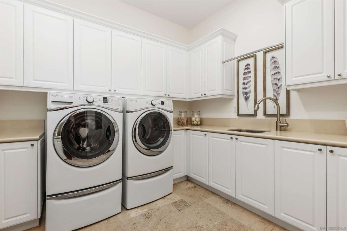 A laundry room with a sink, white cabinets, and a washing machine.