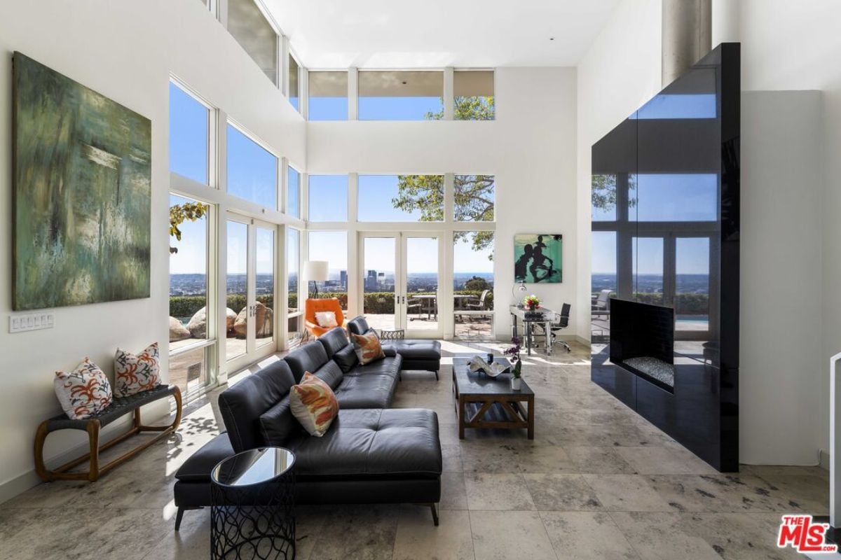 A living room with a fireplace, windows, white walls, black couches, and a center table.