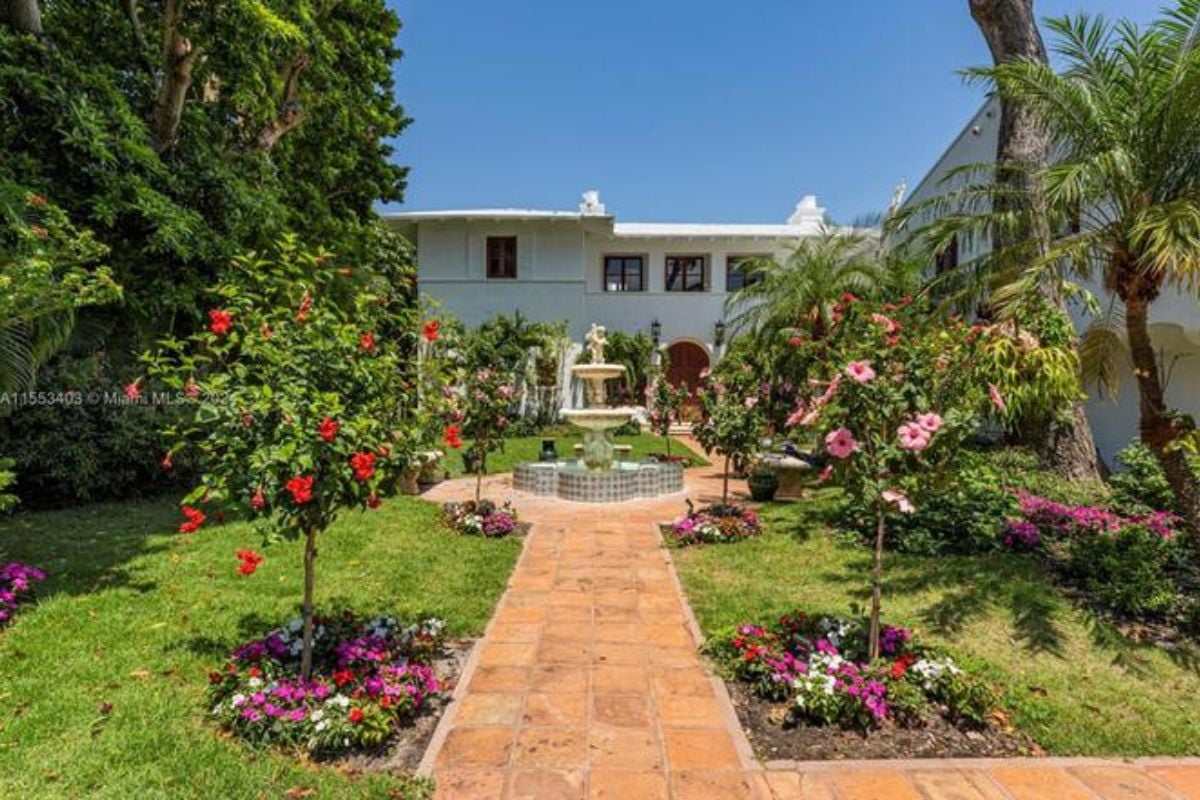 A courtyard with plants, flowers, trees, and a fountain in the middle.