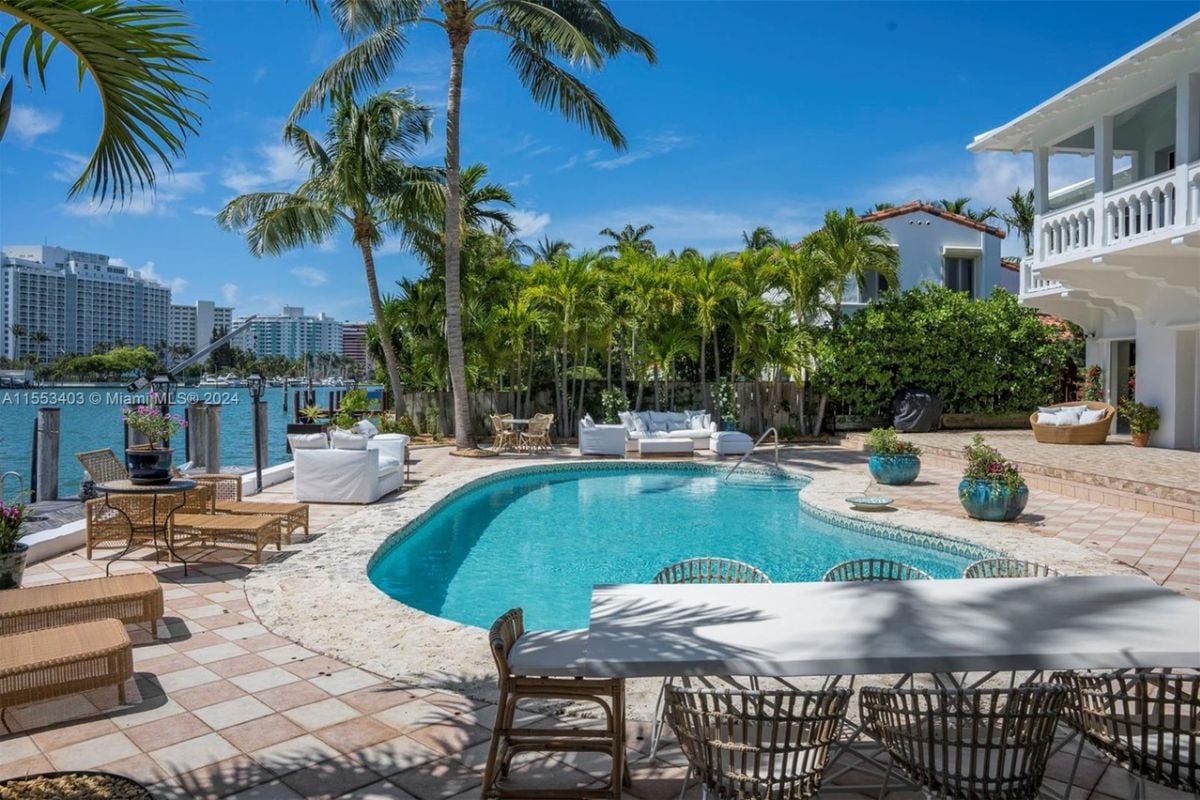 A swimming pool with couches, chairs, plants, and trees on the poolside.