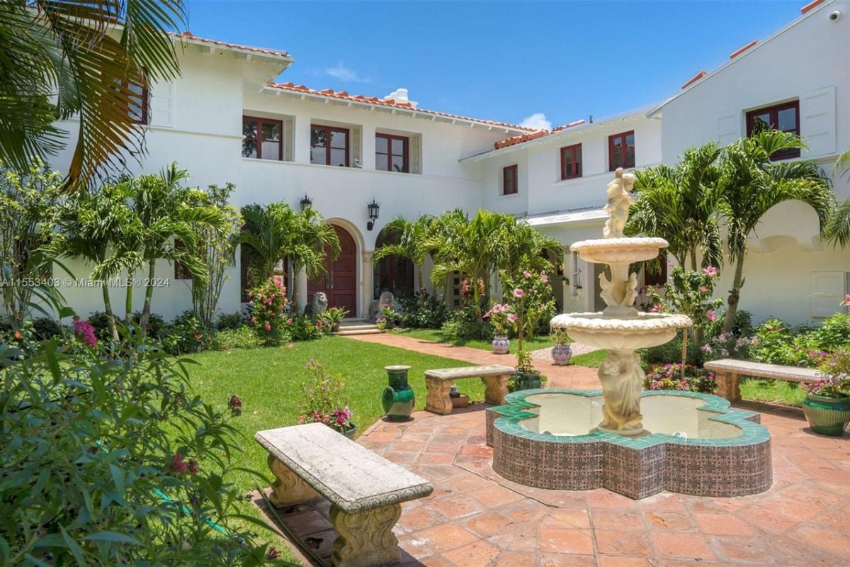 A courtyard with plants, flowers, trees, and a fountain in the middle.