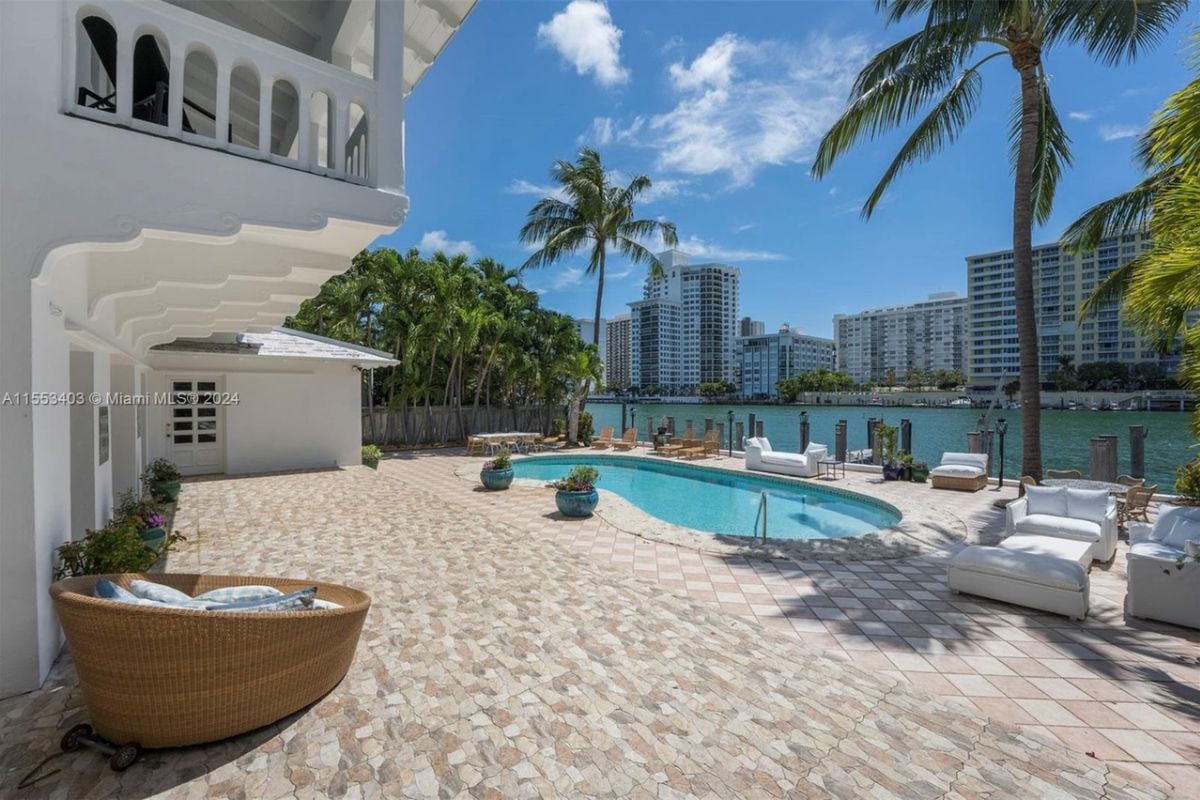A swimming pool with couches, chairs, plants, and trees on the poolside.
