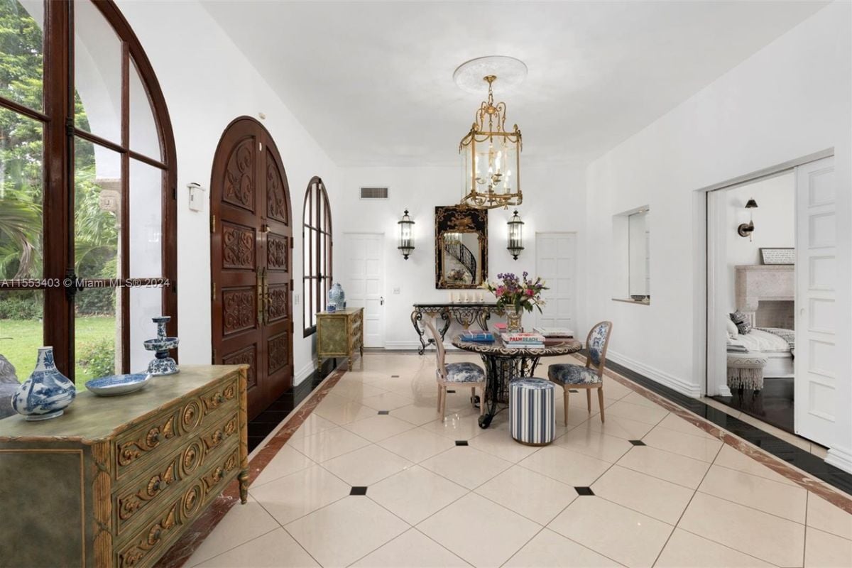 A foyer with a tiled floor, cabinets, a chandelier, windows, a table, and chairs.