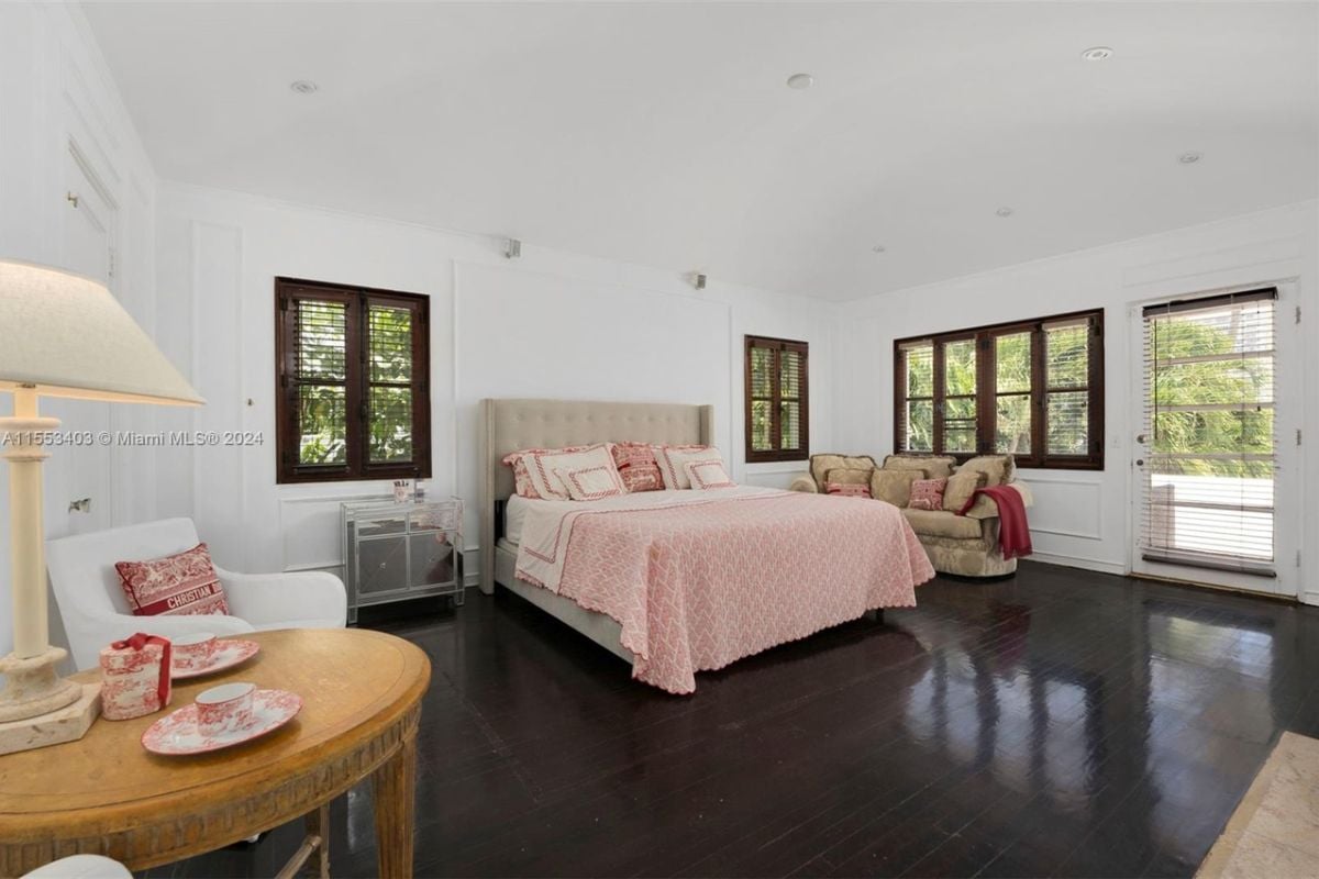 A bedroom with a bed, hardwood floor, couch, windows, and a table.