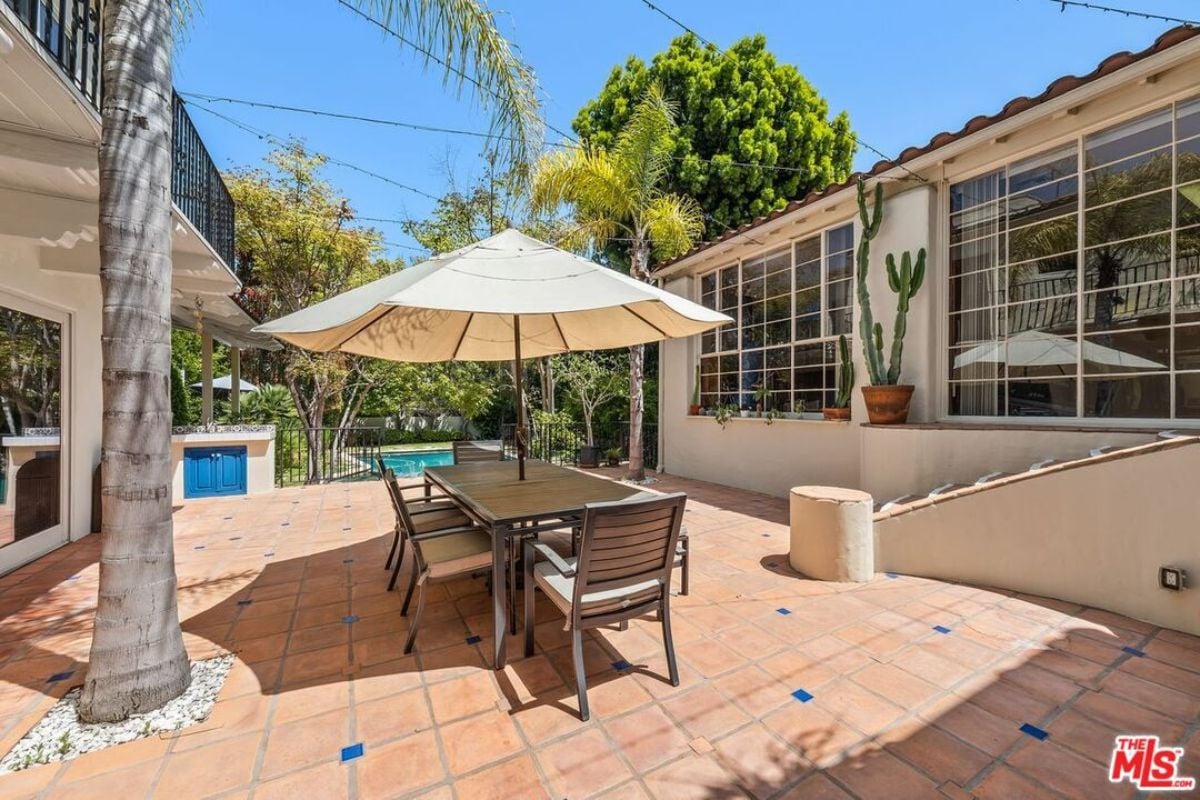 A patio with an umbrella and table surrounded by chairs.