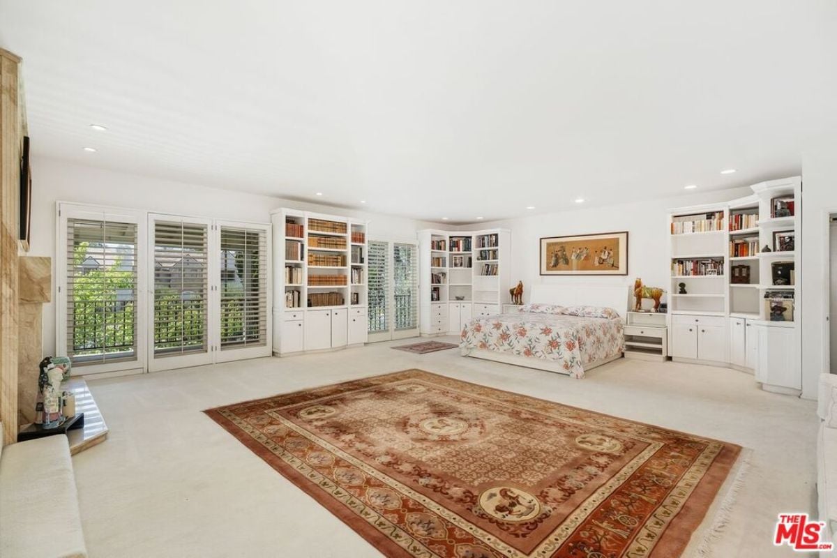 A bedroom with a bed, fireplace, windows, cabinets, shelves, and a rug.