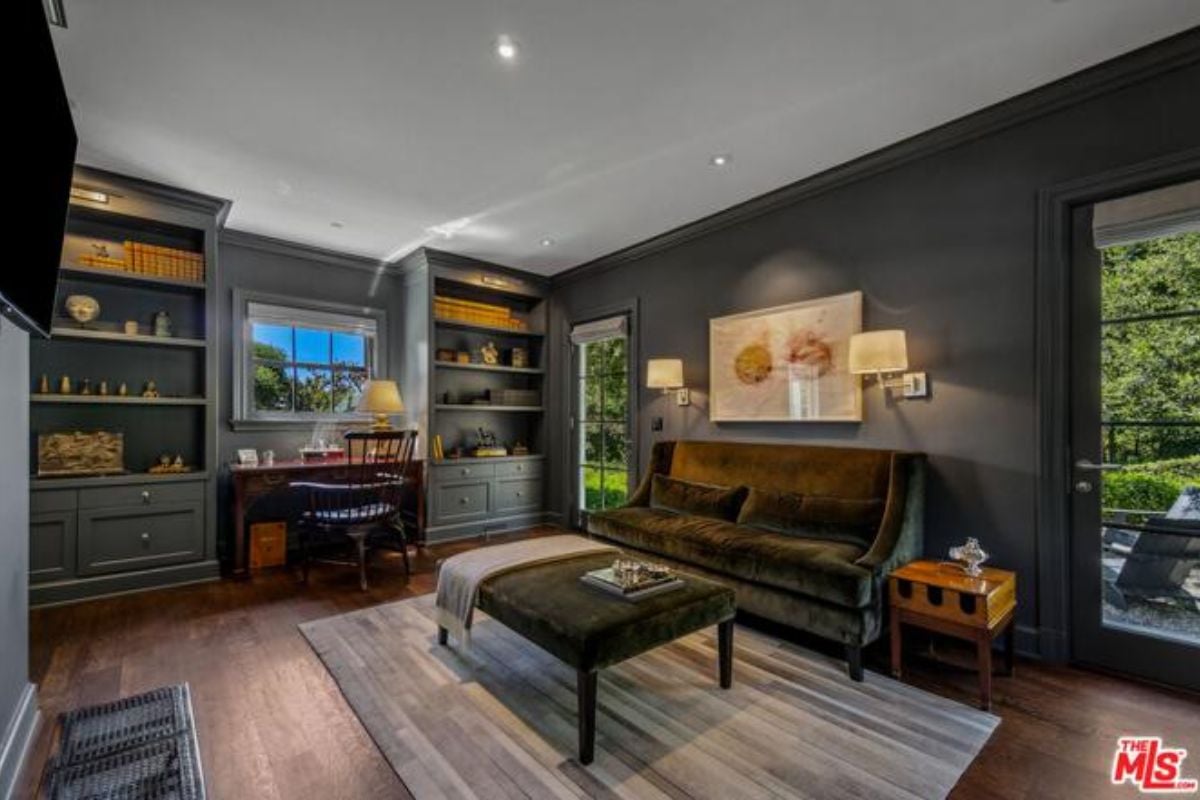A lounge with a hardwood floor, shelves, desk, chair, rug, coffee table, and couch.