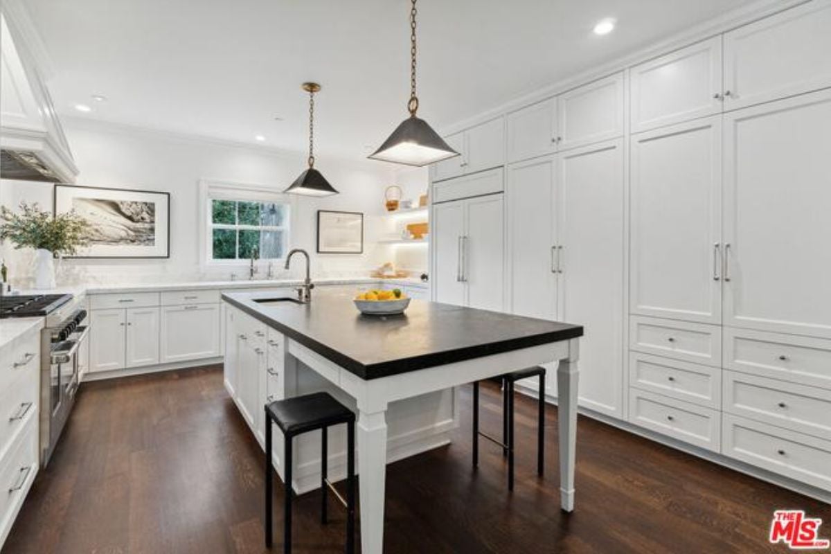 A kitchen with a center island, sink, countertops, white cabinets, and kitchen appliances.