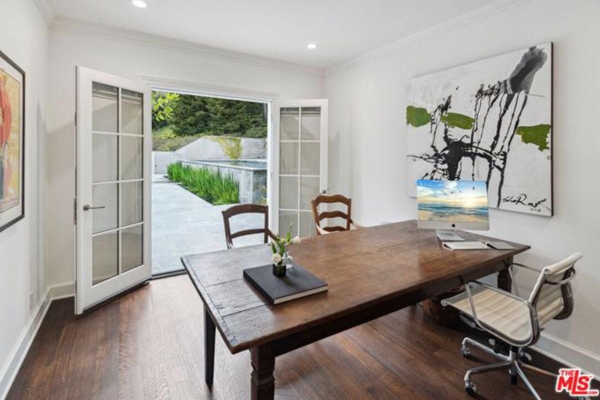 A home office with a hardwood floor, painting, desk, and chairs.