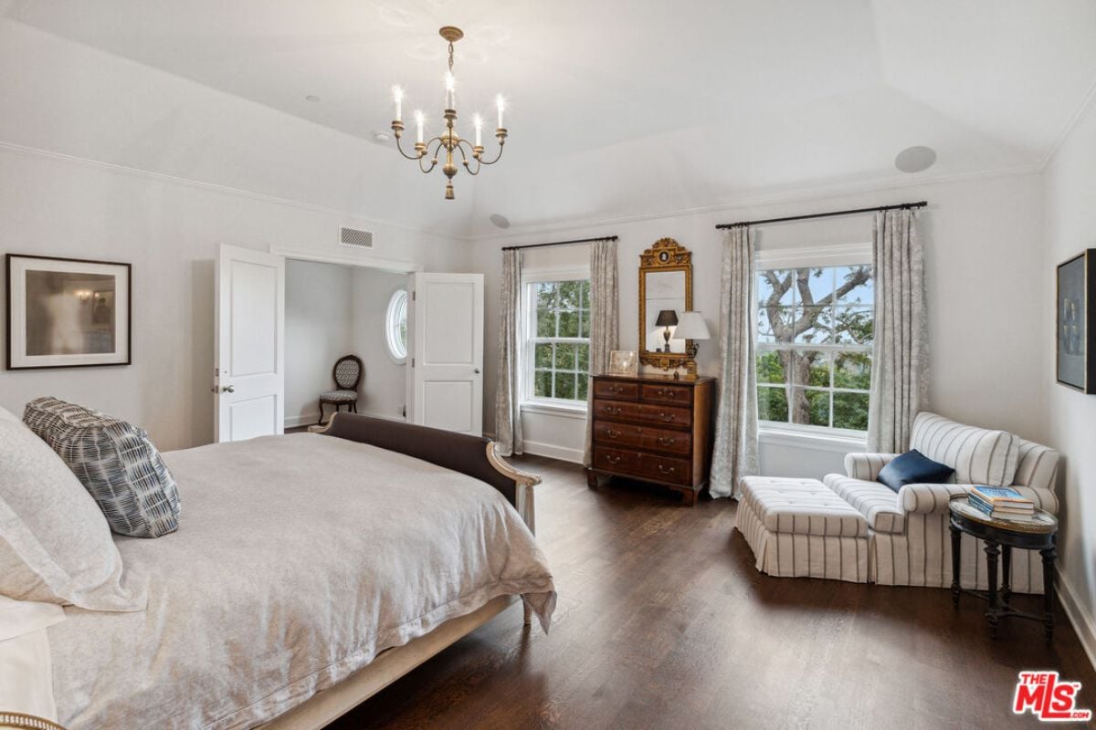 A bedroom with a bed, hardwood floor, couch, mirror, windows, and a cabinet.