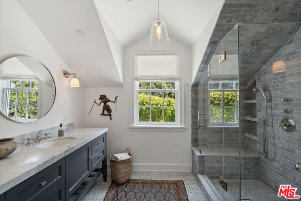 A bathroom with a countertop, mirror, sink, windows, and a shower room.