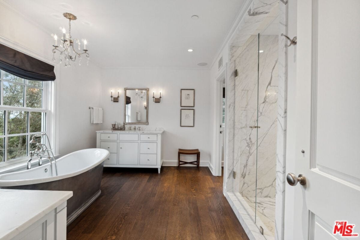A bathroom with a bathtub, window, vanity, mirror, and shower room.