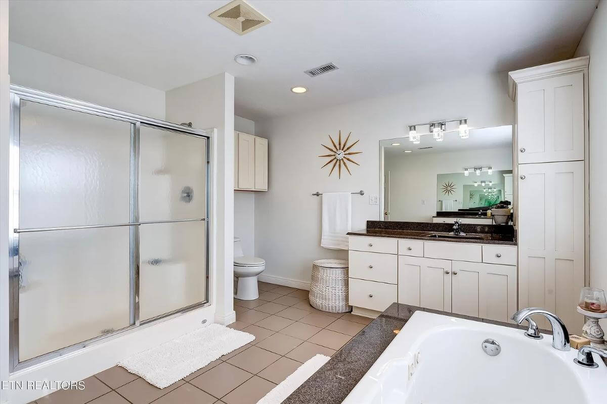 The primary bathroom includes a walk-in shower and a toilet topped with overhead cabinets.