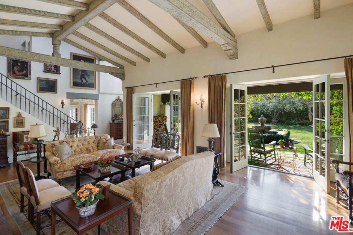 A living room with an exposed beam ceiling, rug, couches, chairs, and a center table.