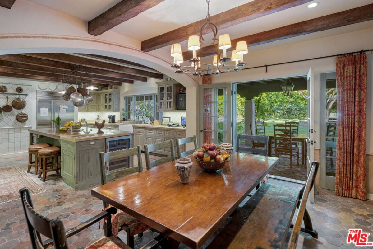 A dining area and kitchen with an exposed beam ceiling, dining table, chairs, bench, island, countertop, sink, and cabinets.