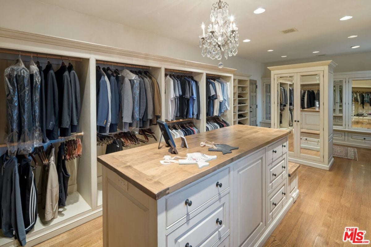 A walk-in closet with a center island, cabinets, drawers, shelves, and a chandelier.